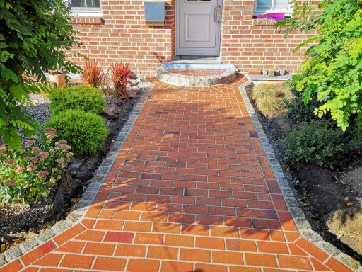 Rot gepflasterter Eingangsweg mit Randsteinen und Grünfläche